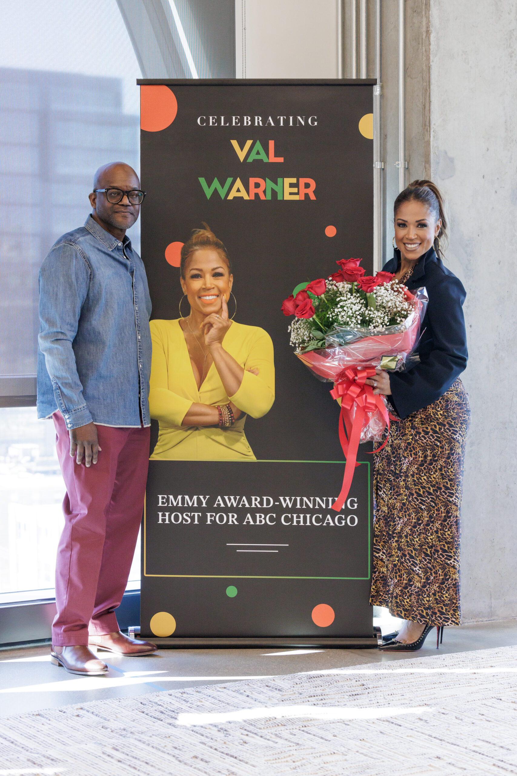Val Warner posing with her BOLD speaker series poster and flowers next to Chip Joseph