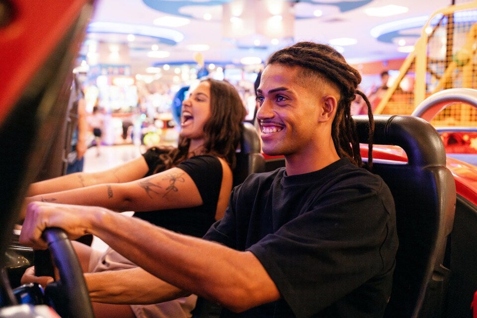 guy and girl at an arcade, playing a driving game