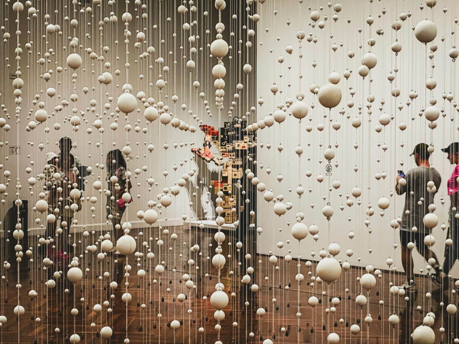 Visitors walking through an art installation of hanging white spheres.