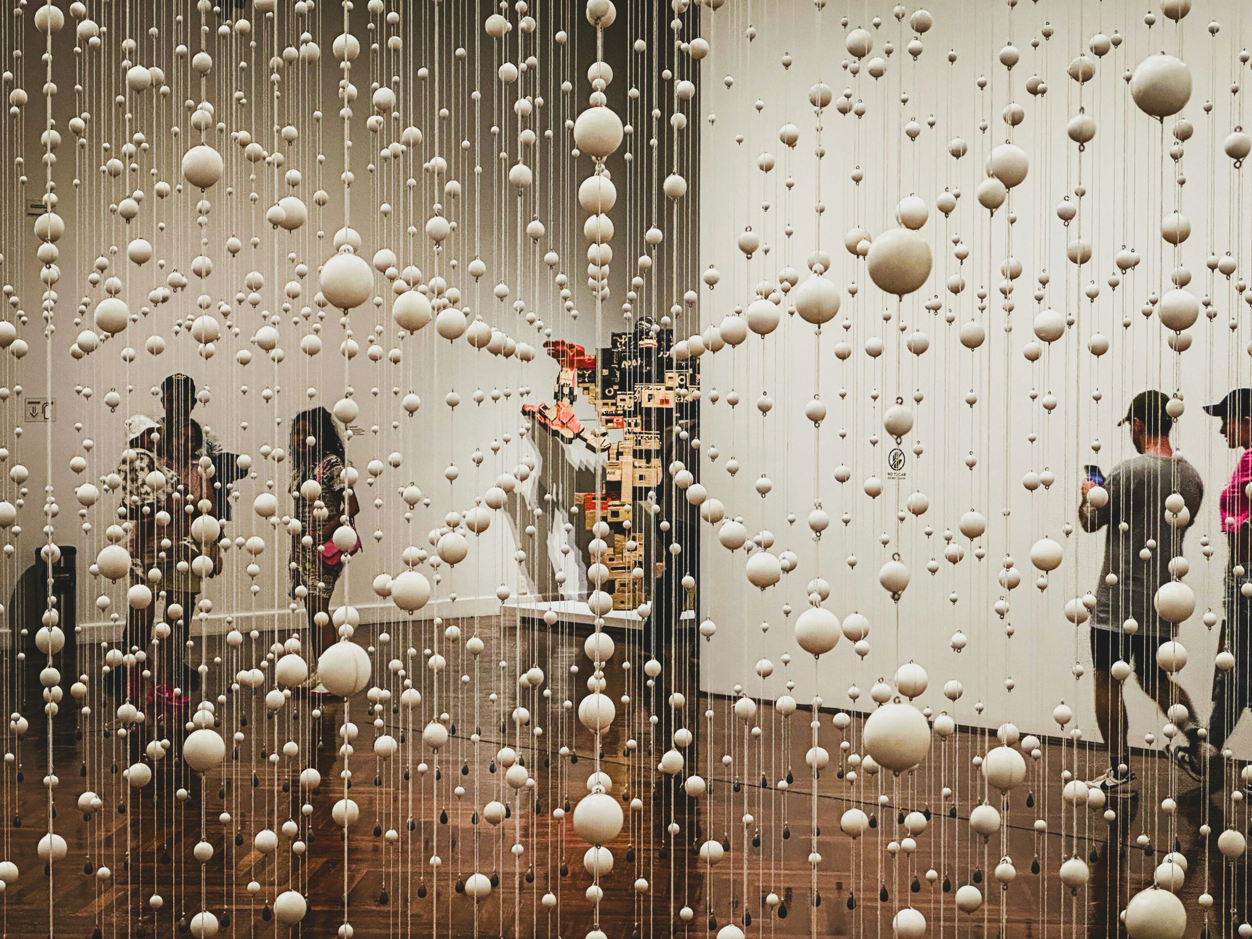 Visitors walking through an art installation of hanging white spheres
