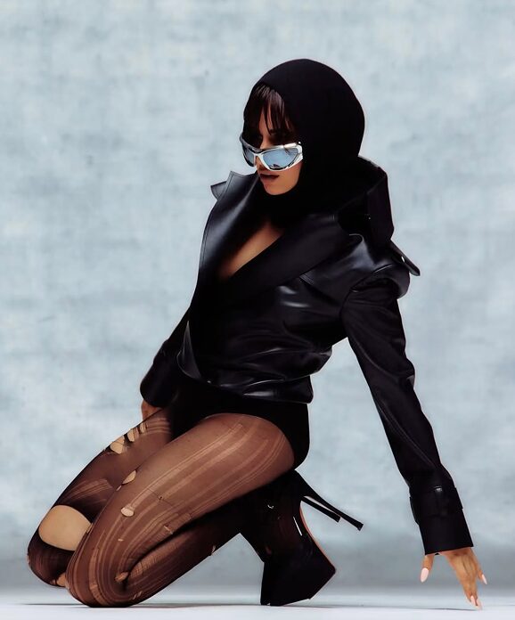Model posing in a black hooded outfit and reflective sunglasses