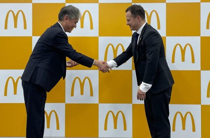 Deux hommes s'inclinant tout en se serrant la main devant le logo de McDonald's lors de la cérémonie de remise des prix.