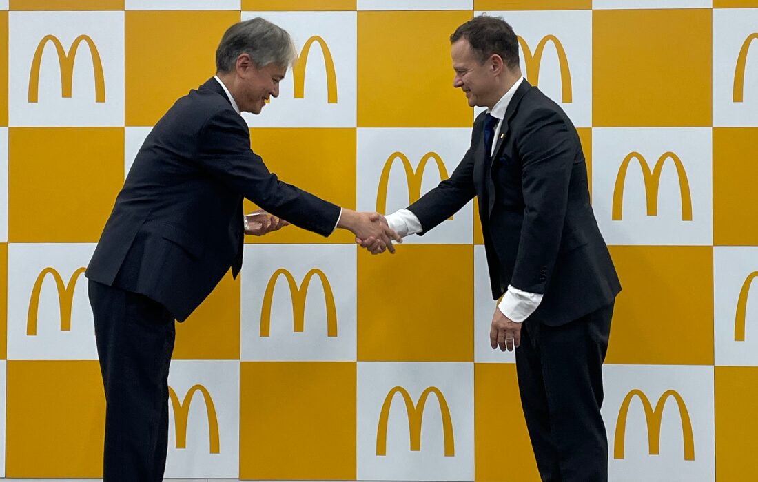 Two men bowing while shaking hands in front of the McDonald's logo at the award ceremony