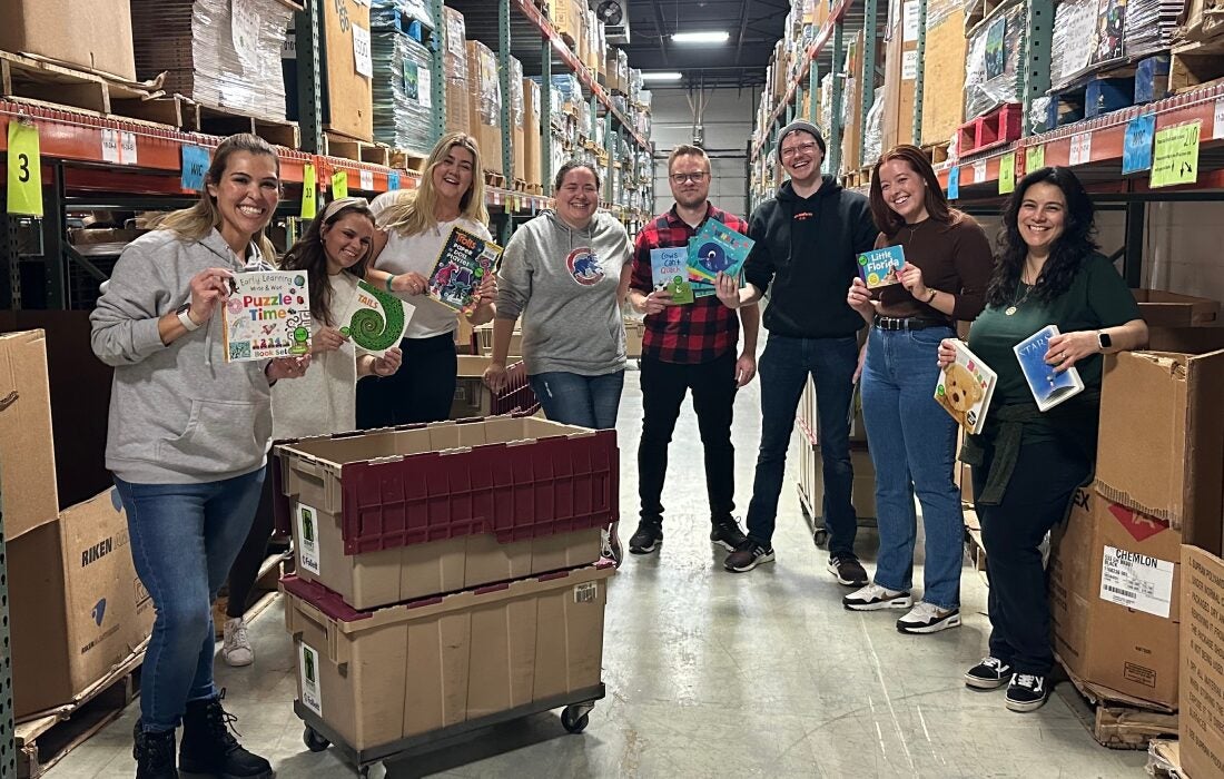 People posing for a photo holding books in the Bernie's Book Bank warehouse