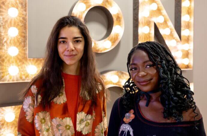 Image de Tara et Nicole souriant à l'appareil photo devant un panneau lumineux "London".