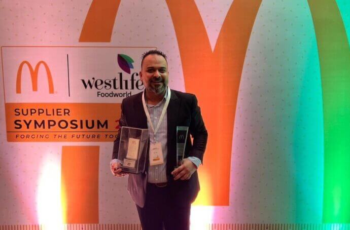 Le lauréat tient son prix lors du symposium des fournisseurs en Inde, devant une enseigne McDonald's.