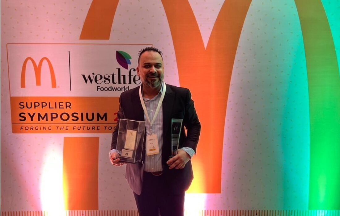 The recipient holding the award at the India supplier symposium in front of a McDonald's sign.