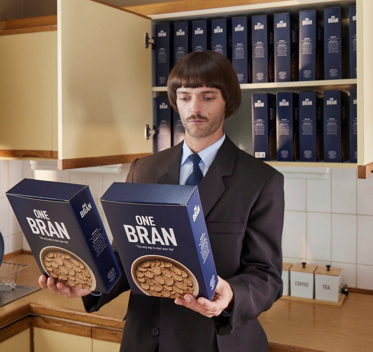 man in kitchen holding two cereal boxes