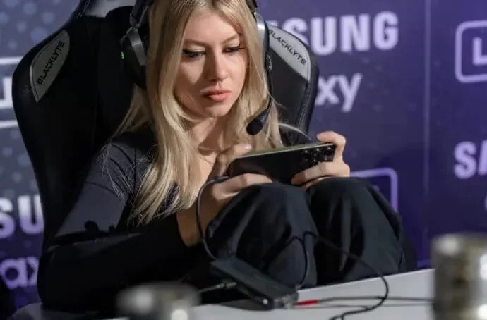 A person wearing headphones sits in a gaming chair while playing a game on their mobile device.