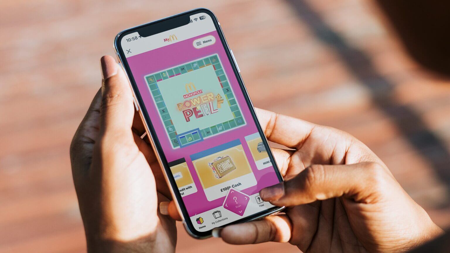 Mains tenant un iPhone avec l’écran d’introduction du jeu Monopoly Power Peel