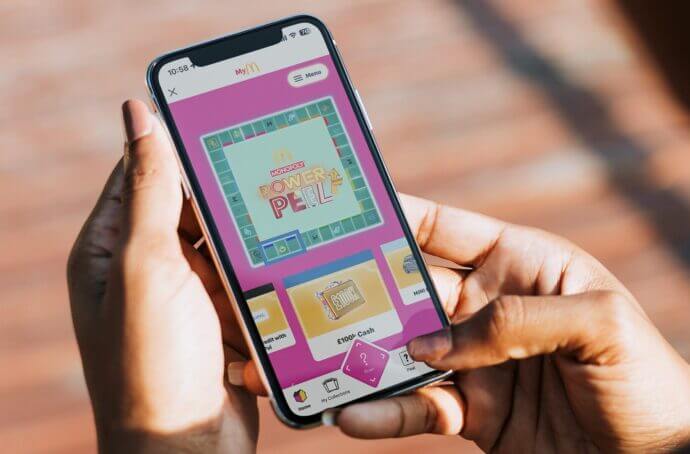 Mains tenant un iPhone avec l’écran d’introduction du jeu Monopoly Power Peel