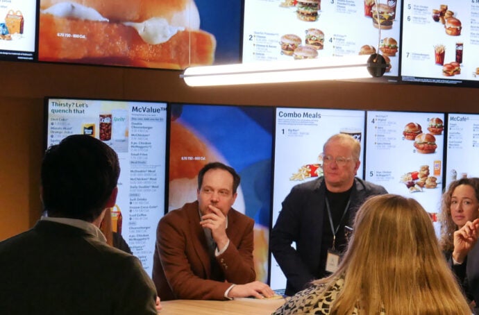 A group of people gathered around a table inside a McDonald’s restaurant. Several digital menu boards are displayed behind them.
