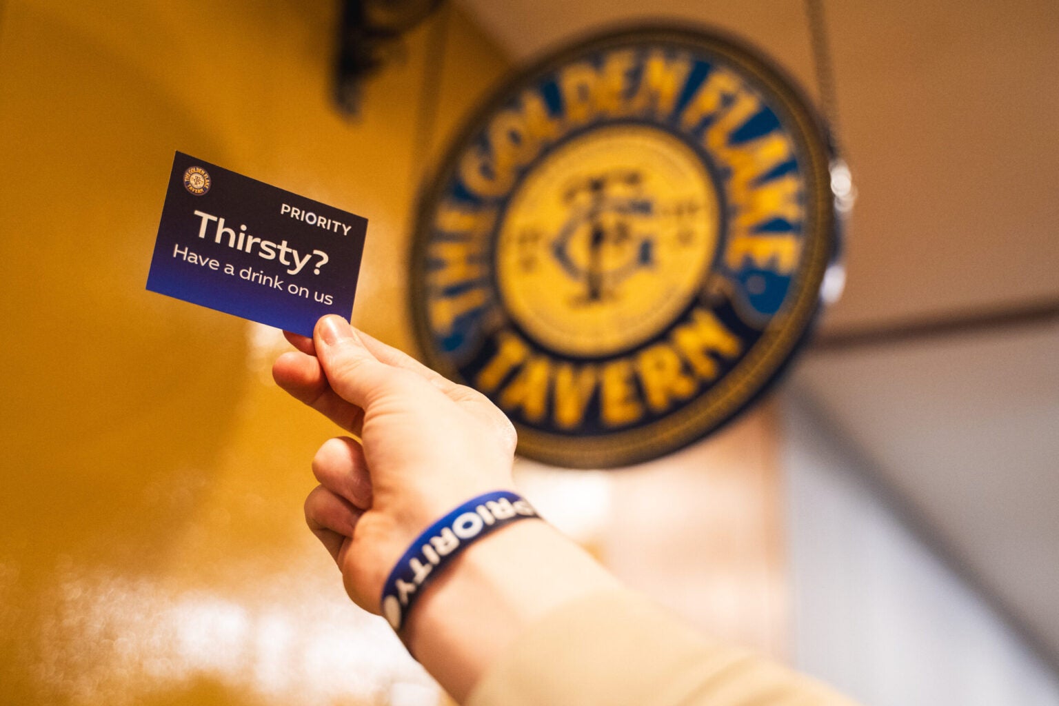 A picture of the Golden Flake Tavern logo with a hand holding a Priority notecard