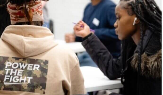 A woman in a hoodie with the "Power the fight logo" on the back next to another woman