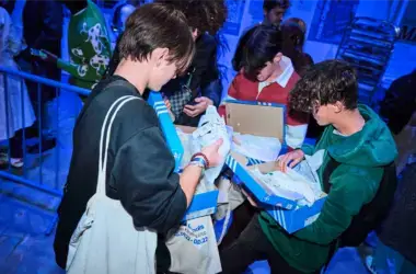 A group of people stand in a circle opening boxes of shoes at a Adidas event.