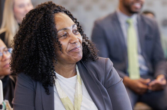 A woman sitting among a group of people, smiling and listening during what appears to be a meeting or presentation.