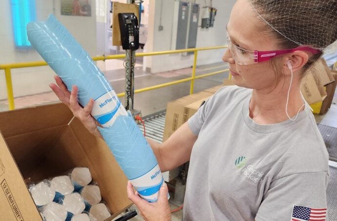 A factory worker wearing personal protective equipment inspects a stack of McFlurry packaging.