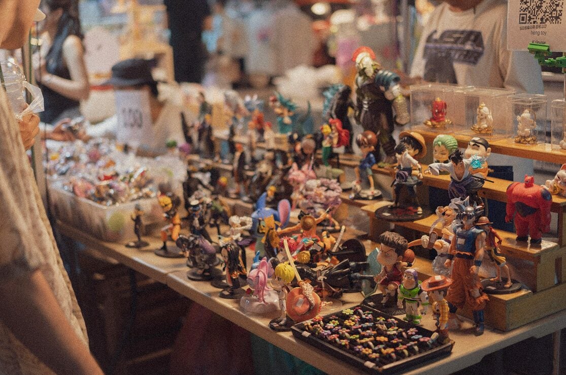 Table of anime and pop culture figurines displayed at a busy market stall.