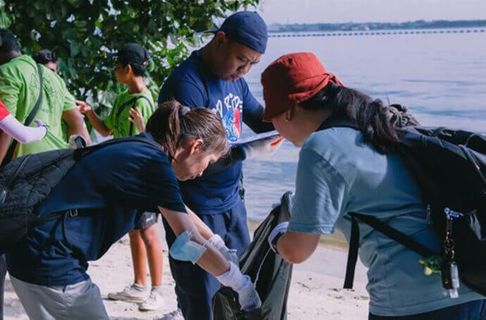 Des personnes travaillant ensemble lors d’un nettoyage de plage, portant des gants et déposant les déchets ramassés dans un grand sac près du rivage.