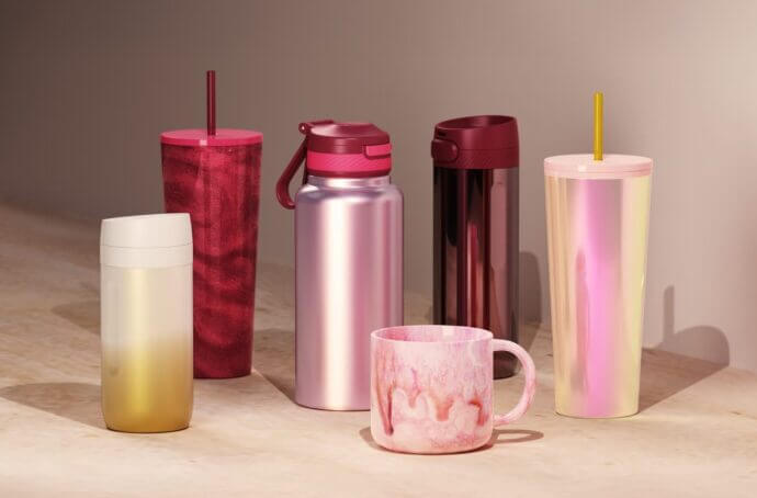 A collection of drinkware items arranged on a tabletop, including tumblers, bottles, and a mug in shades of pink, red, gold, and iridescent finishes.