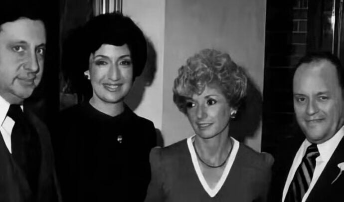 Four people pose together in a black and white photo, all dressed in formal clothing. Two women stand in the middle, with two men on either side.