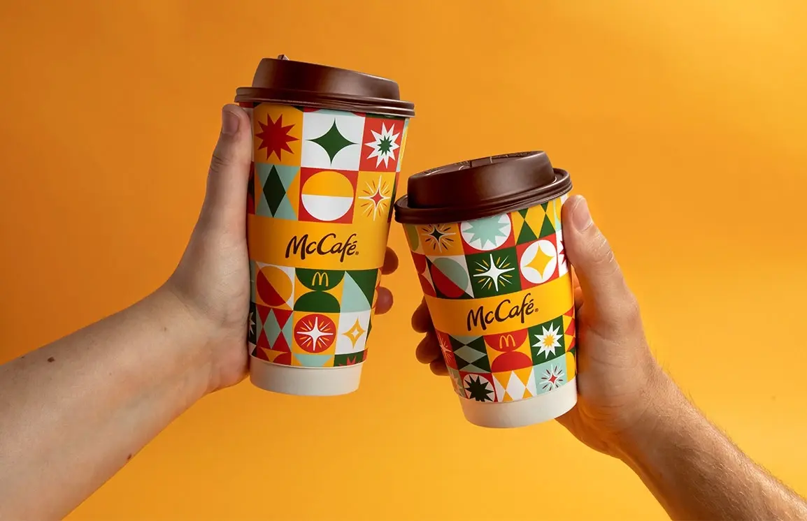2 hands holding the McCafé holiday cups in front of a yellow background