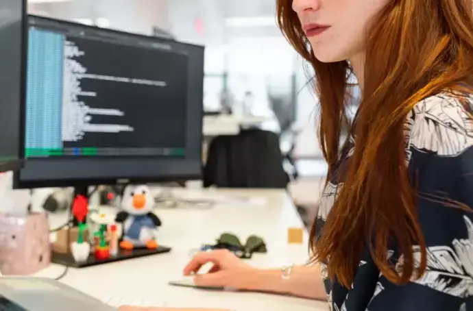 Red-headed woman works on code across three monitors