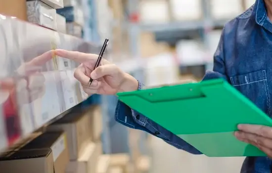 Une personne munie d'un presse-papiers vert montre un article sur une étagère.