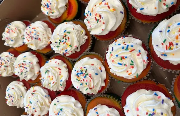 A box of rainbow cupcakes with white frosting and rainbow sprinkles at the event