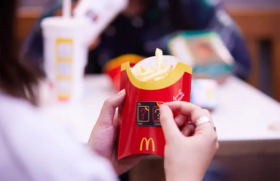 Une personne en train de décoller le logo Double Peel de la boîte de frites de McDonald's