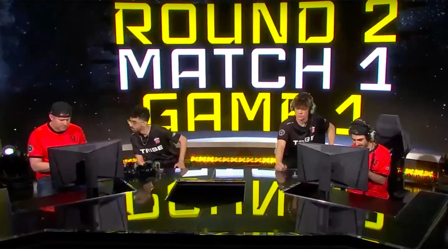 4 gamers behind 2 computer screens and yellow and black background that says 