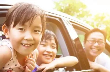 Un homme et deux enfants dans une voiture noire qui passent leur tête par la vitre en souriant