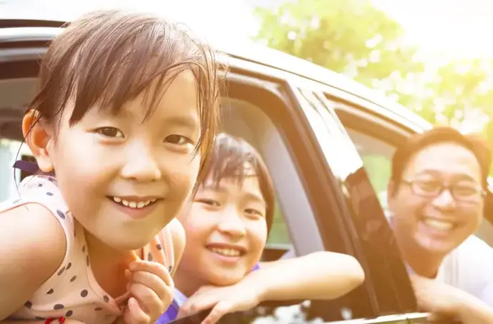 Man and two children smiling, leaning out the windows of black car