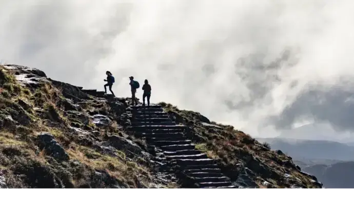 One person leading two others up a mountain